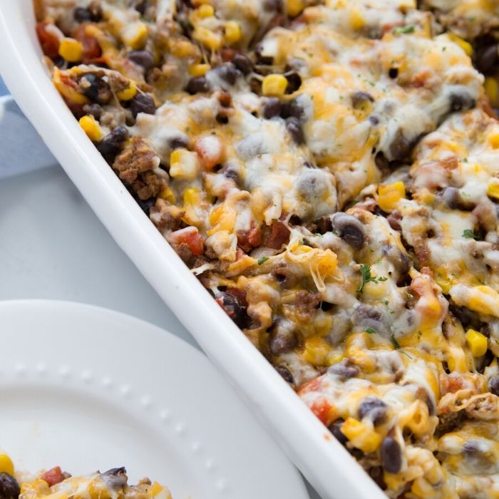 cheesy taco bake in casserole pan with plate of some by it 