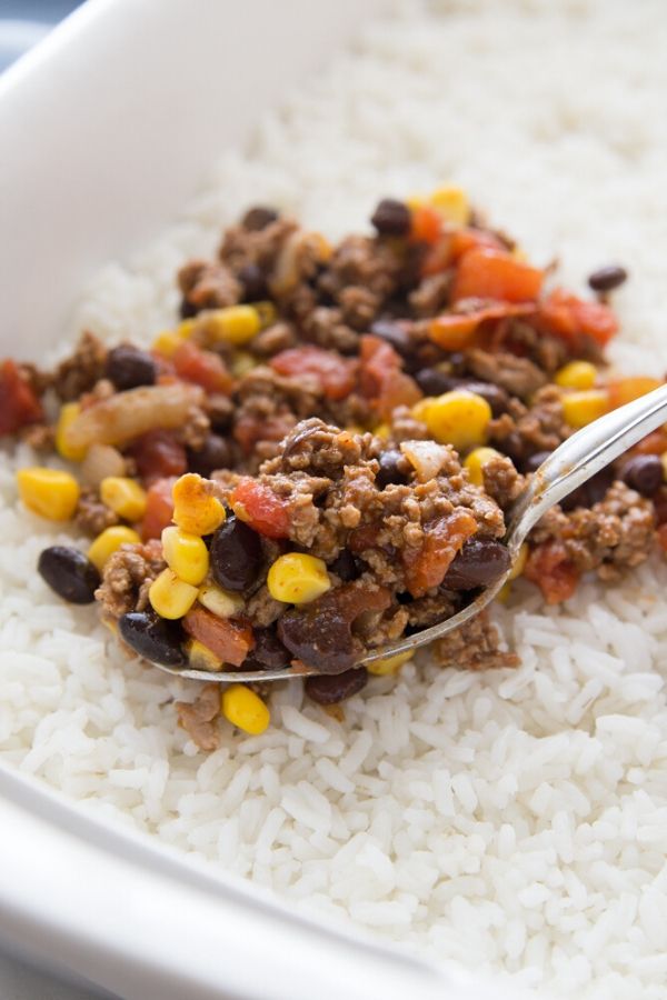 pouring tex mex meat mixture over the top of a bed of rice