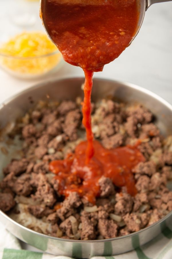 salsa being poured into pan with ground beef 