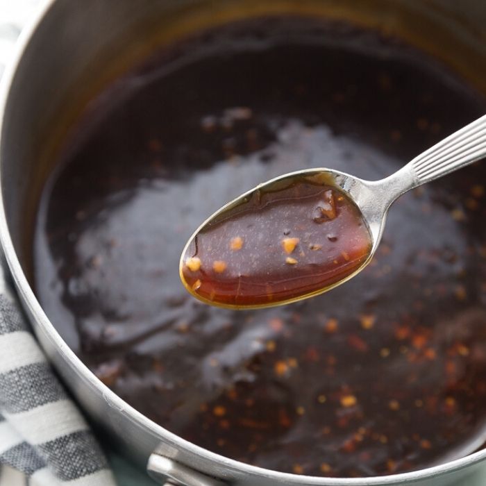 cashew chicken sauce in a pan with a spoon full of it 