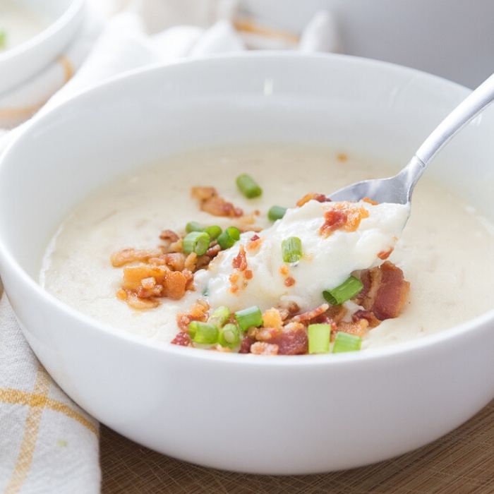 bowl of potato soup topped with bacon and green onions with spoon in it