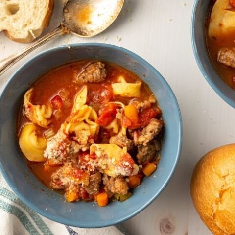 tortellini soup in bowls on table with bread by it
