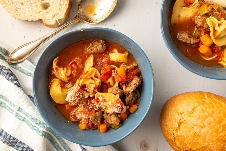 tortellini soup in bowls on table with bread by it