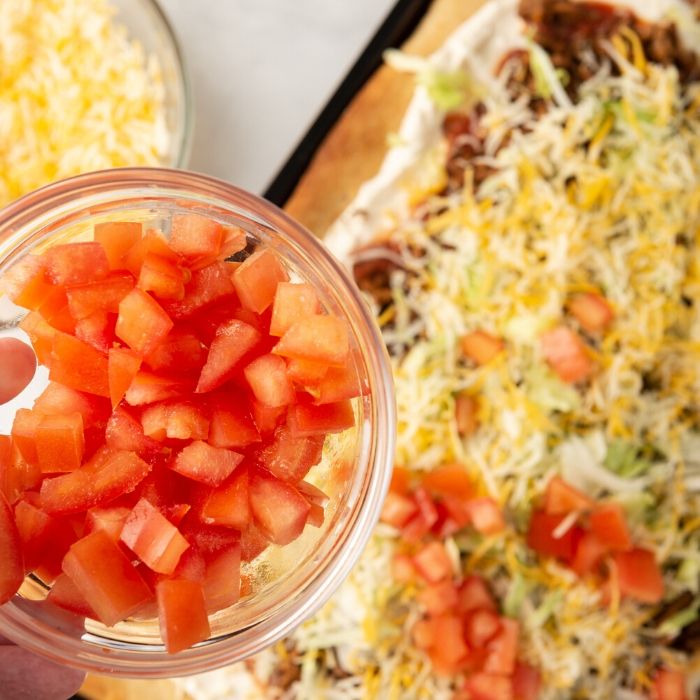 homemade taco pizza getting topped with tomatoes