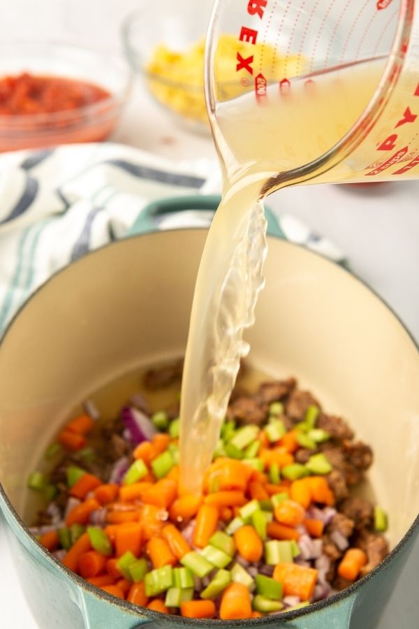 meat and veggies in a pot with broth being poured in 