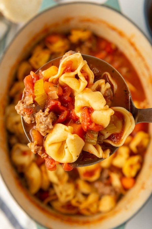ladle with tortellini soup and pot beneath it