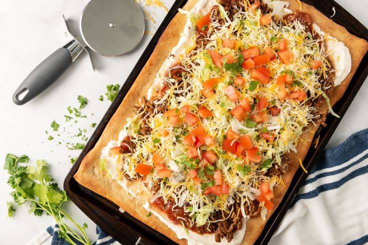 oven baked taco pizza on pan with cutting roller by it