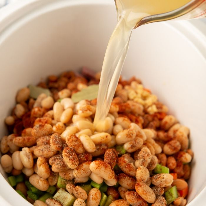 pouring broth in slow cooker with ham and bean ingredients