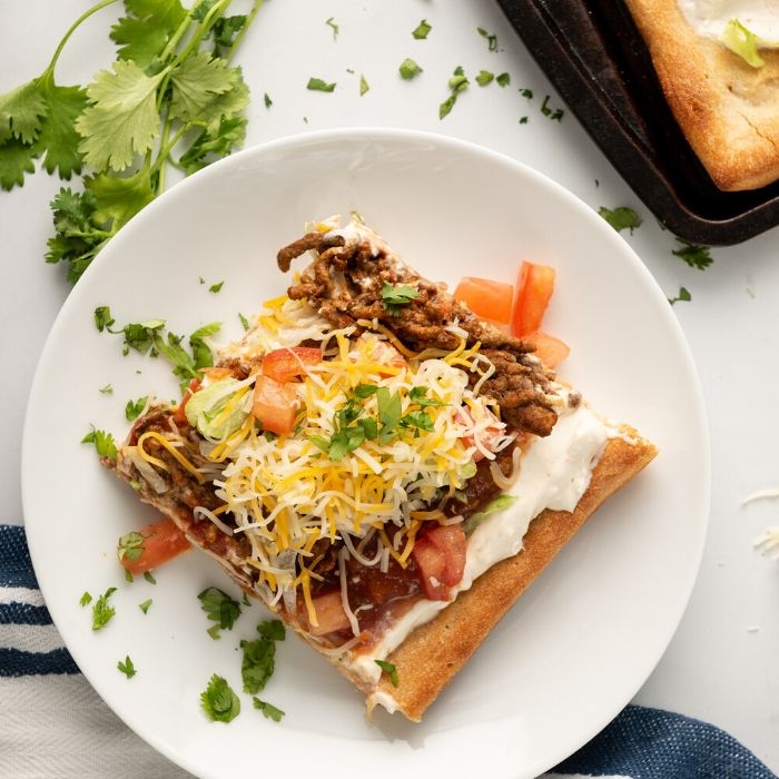 taco pizza on a plate with cilantro on side