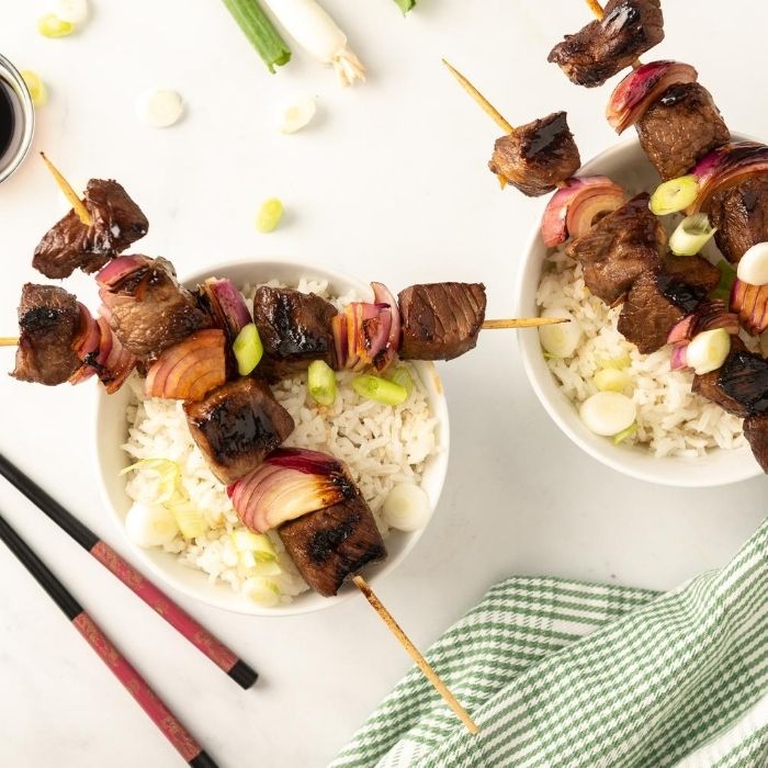 steak skewers on top of a bowl of rice with green onions around it