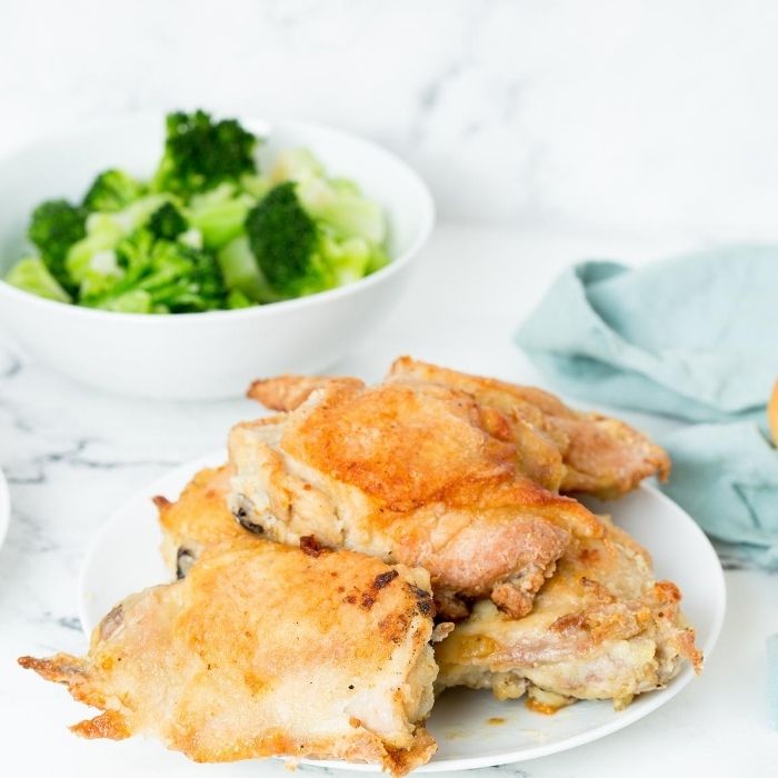 chicken on a plate with broccoli in a bowl behind it 