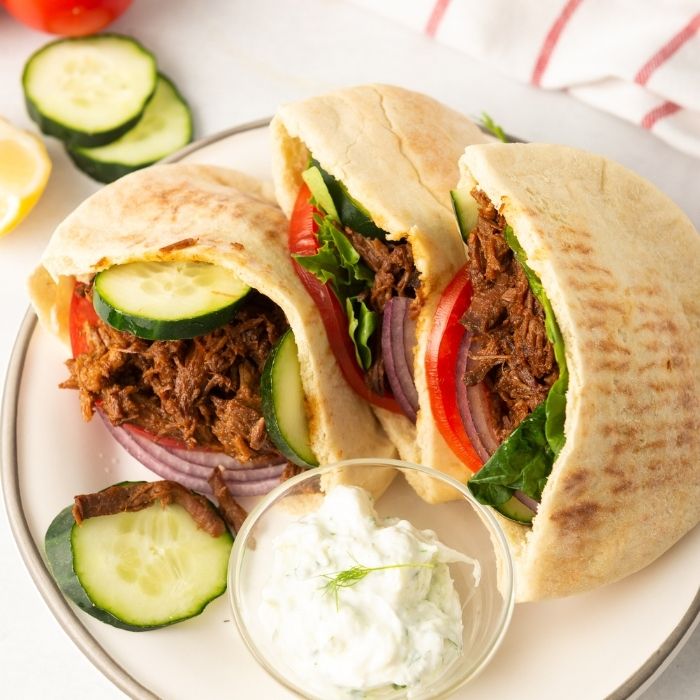 beef gyros on a plate with sauce in a bowl 
