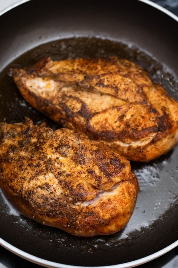 cooking seasoned chicken in a skillet on stove 