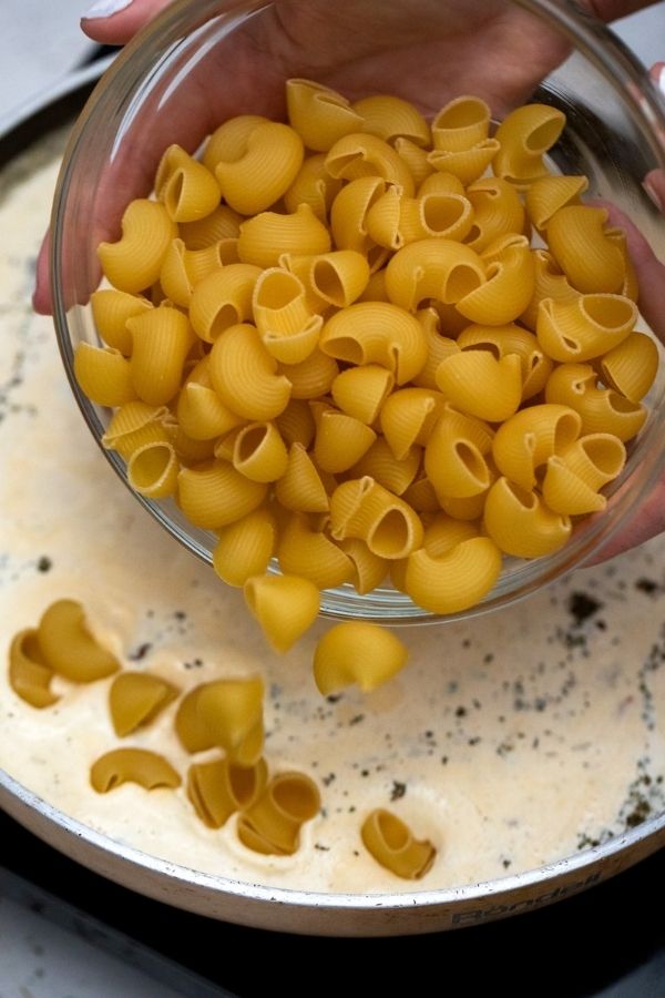 pasta pouring into cheesy sauce on pan