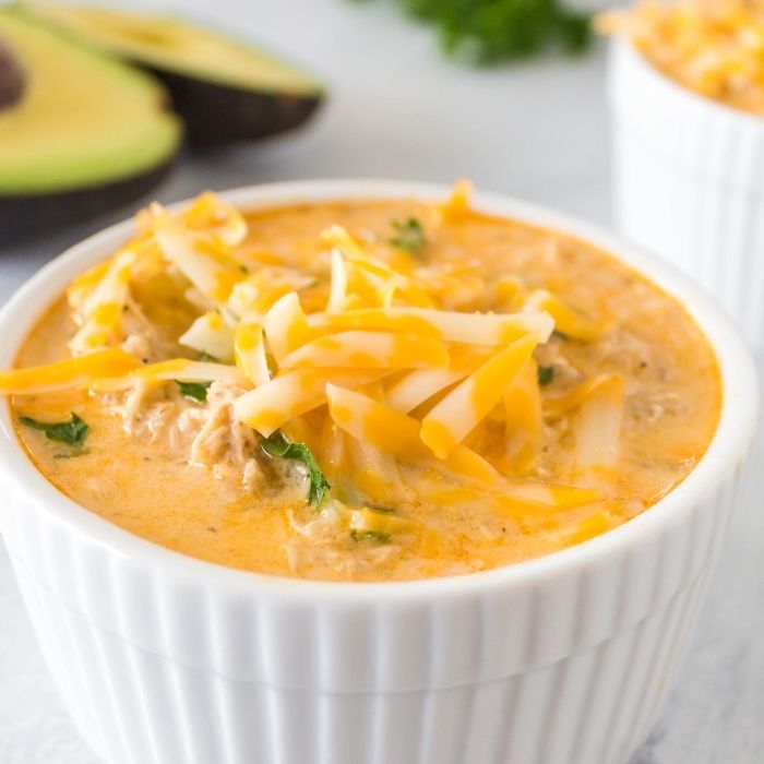 creamy chicken soup in white bowl on table with avocado behind it