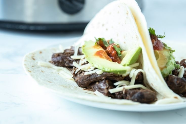 carnitas on a plate with slow cooker behind it