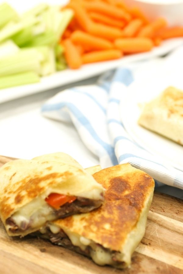 easy philly cheesesteak on wood cutting board and vegetables behind him 