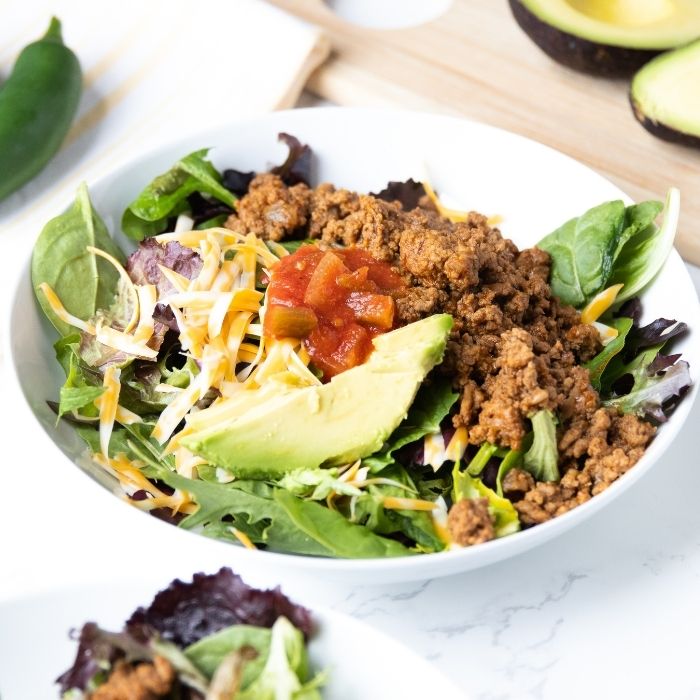 taco salad in a bowl with avocado on counter behind it 