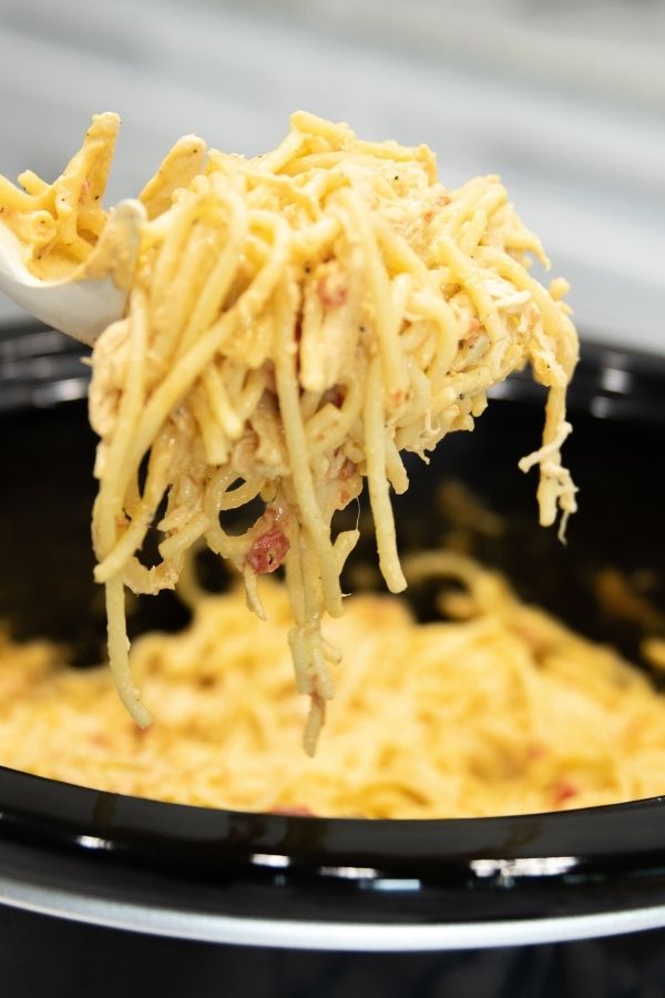 spoon holding up chicken pasta above slow cooker 