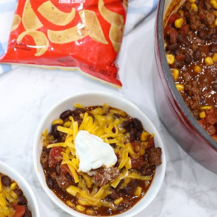 pot and bowl with black bean chili and bag of frito chips by it 