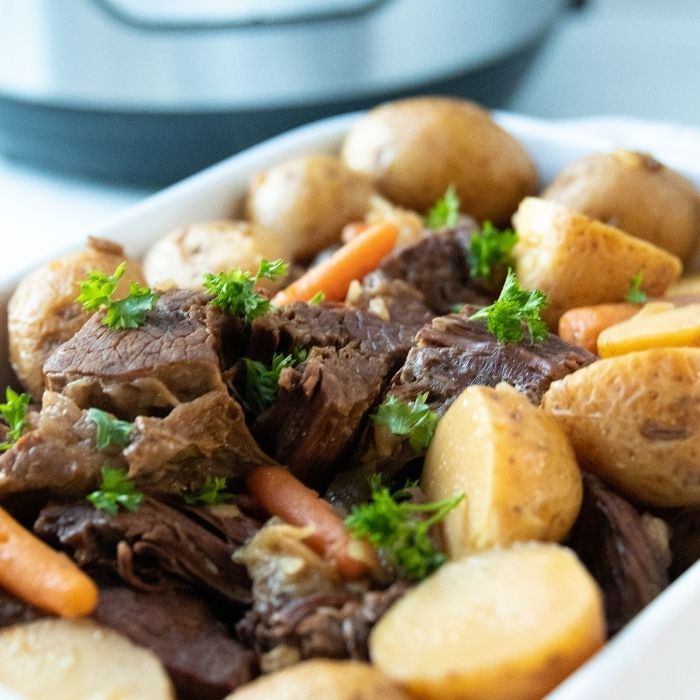 roast and vegetables in a white casserole pan