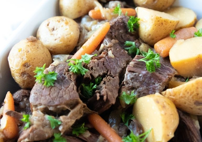 pan with pot roast and vegetables in it garnished with greens