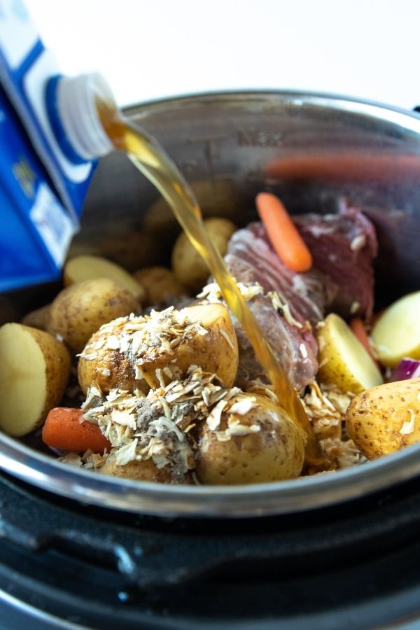 broth being poured into instant pot with pot roast and vegetables 